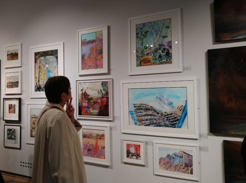 Woman reflecting on Cathy Read paintings at the Mall Galleries in London
